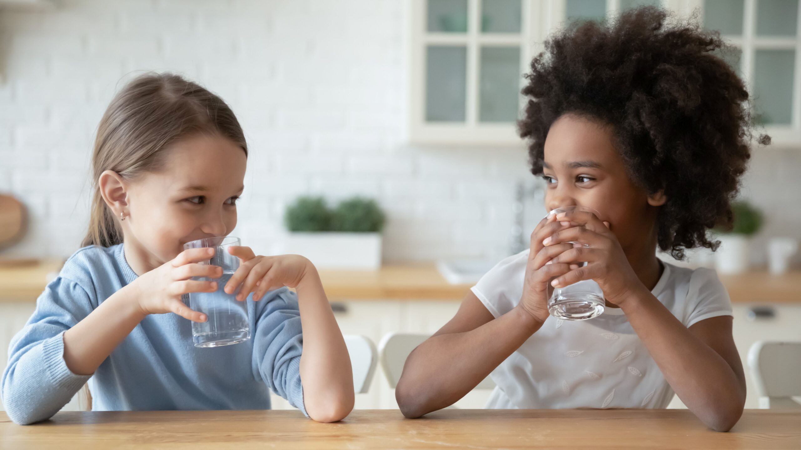 Zwei Kinder trinken sauberes Wasser und lächeln sich an